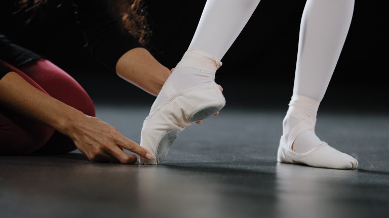 Ballet teacher helping a dancer with foot and turnout alignment.