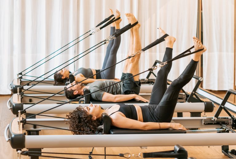 Patients performing guided Pilates reformer exercises in a studio setting.
