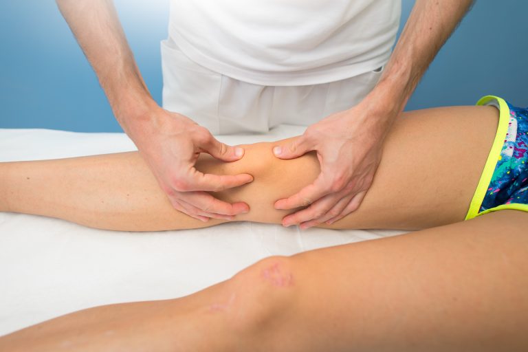 Physical therapist performing patellar mobilization on a patient's knee.
